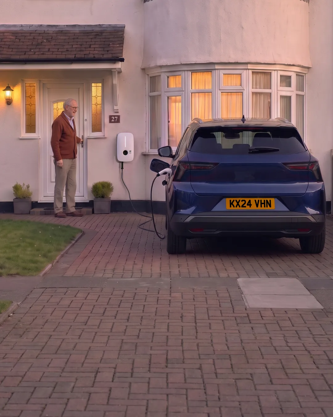 Dusk. Martin at his front door, his own car plugged in on the drive for the night.