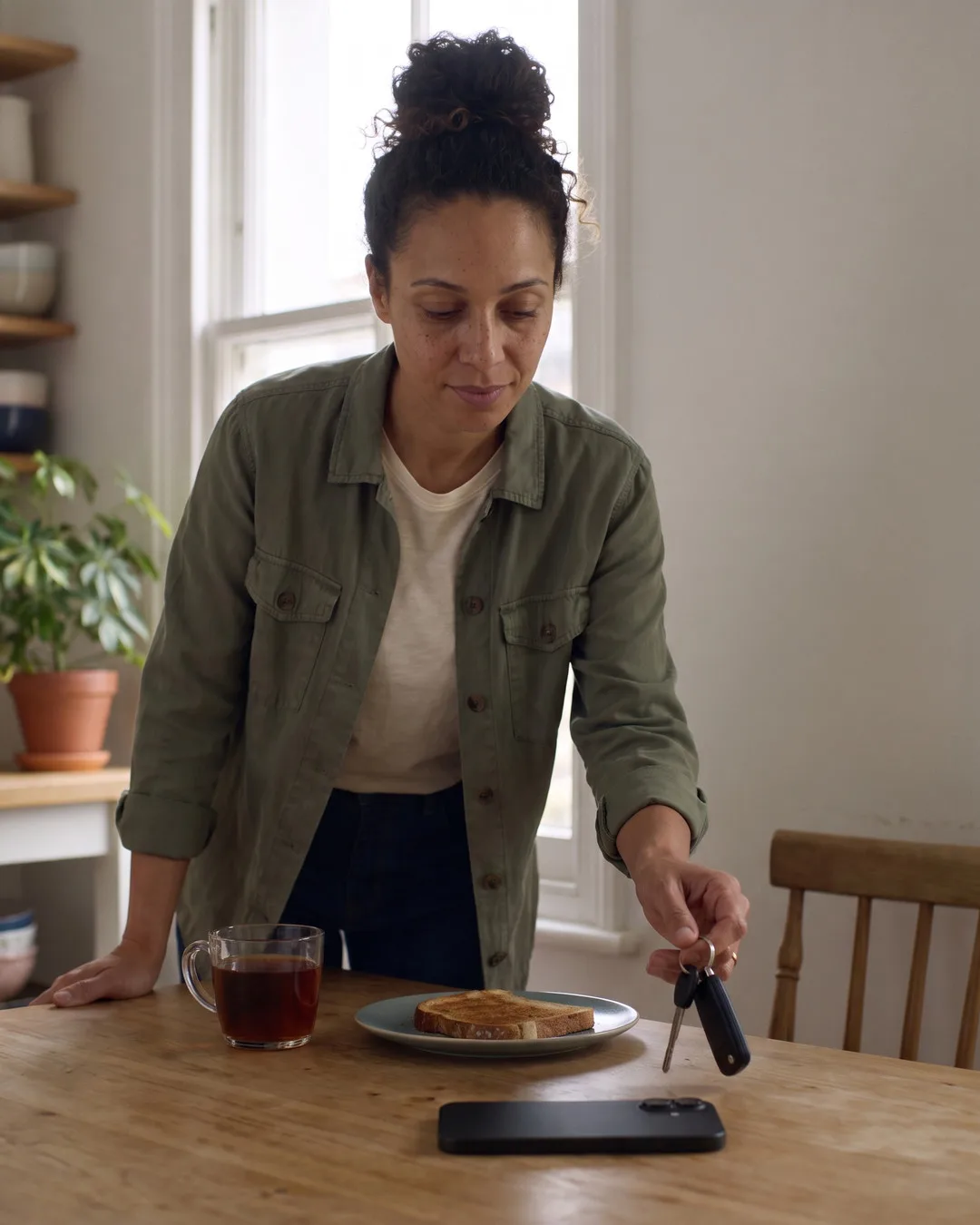 Maya at her kitchen table, her phone face down, picking up her keys.