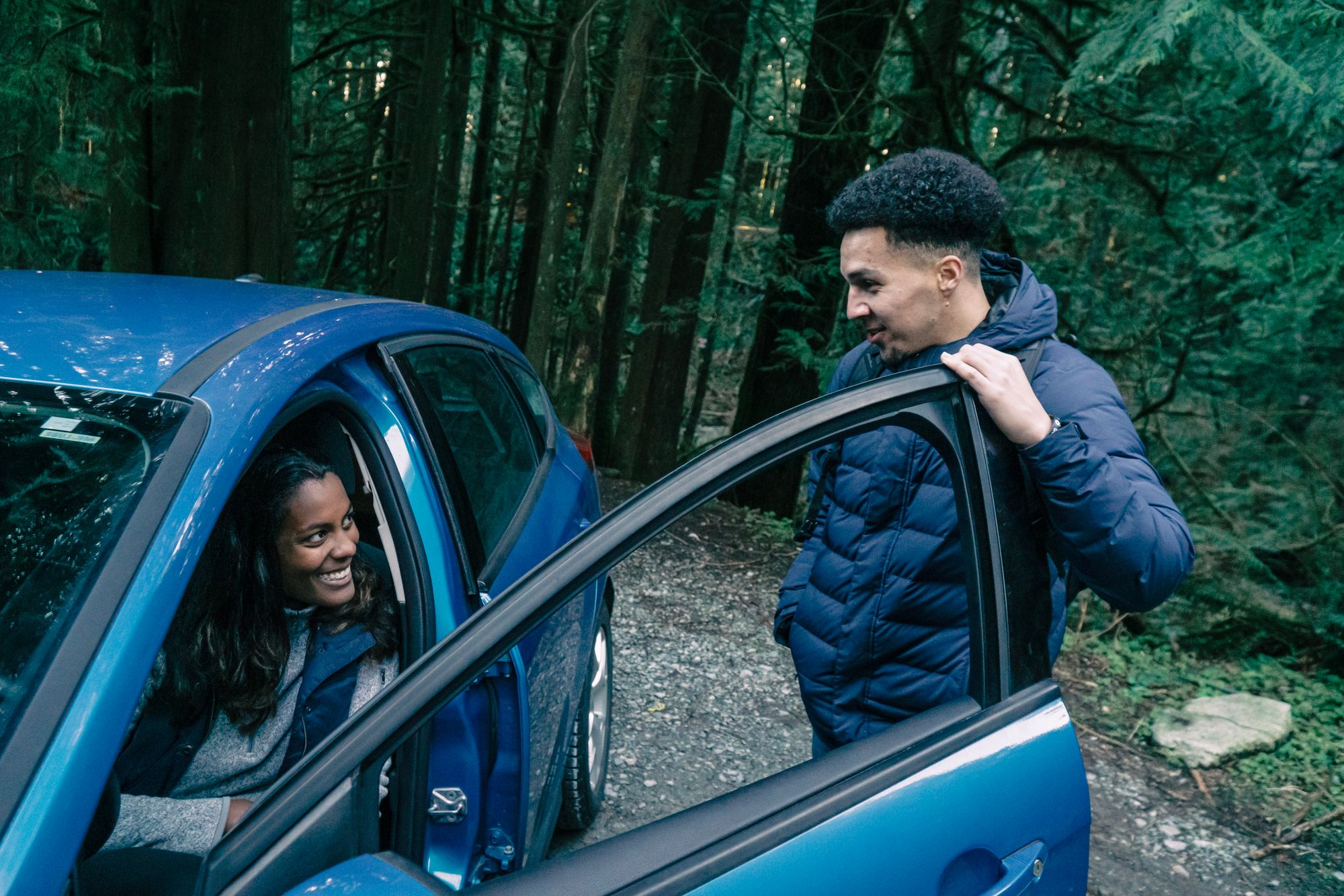 Two people talking beside a parked car.